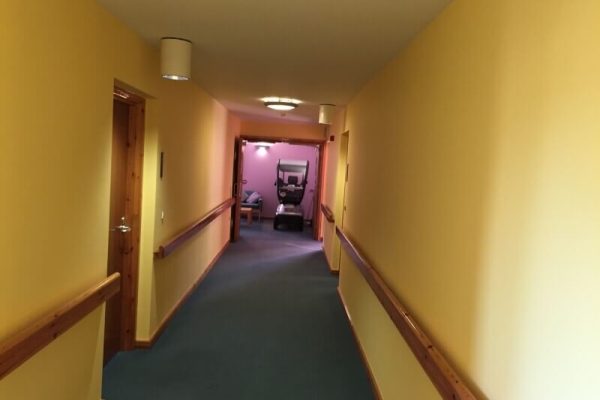 room painted yellow with wooden handrails and doors. at the end of the hallway, there is a door opening into another hallway painted purple